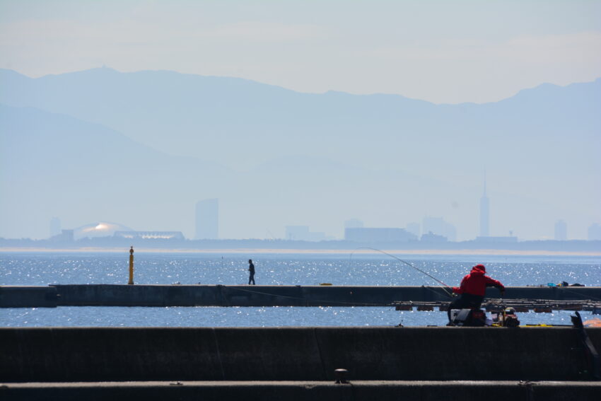 相島の漁港で釣りをする人々と遠くに福岡市街