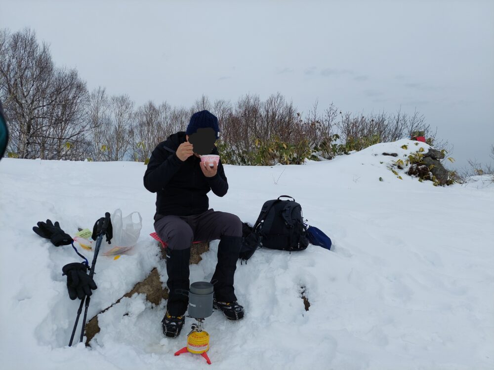 冬の飯綱山山頂で昼飯を食べる登山者