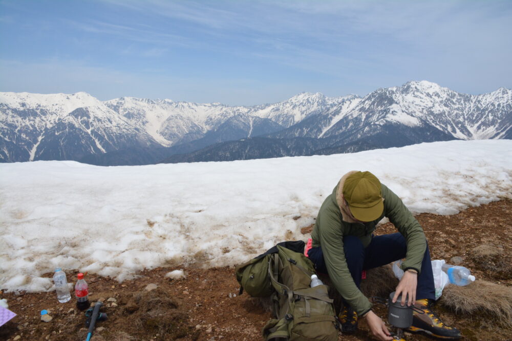 残雪期の焼岳南峰山頂で昼飯を食べる登山者