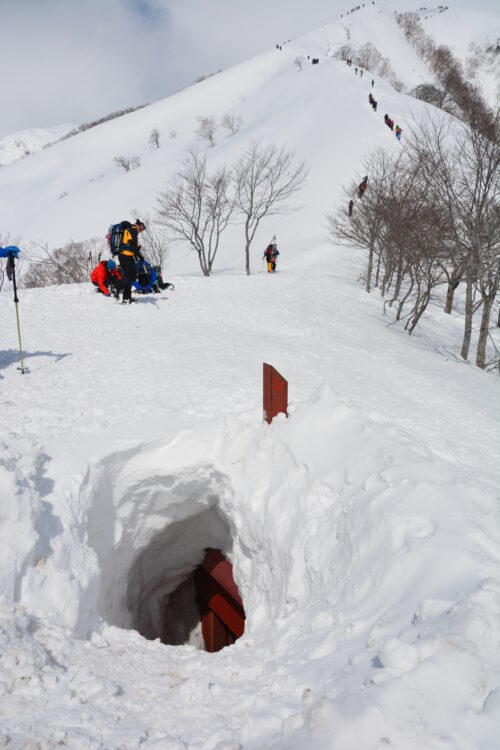 冬の谷川岳登山道を歩く登山者たちと埋もれた避難小屋