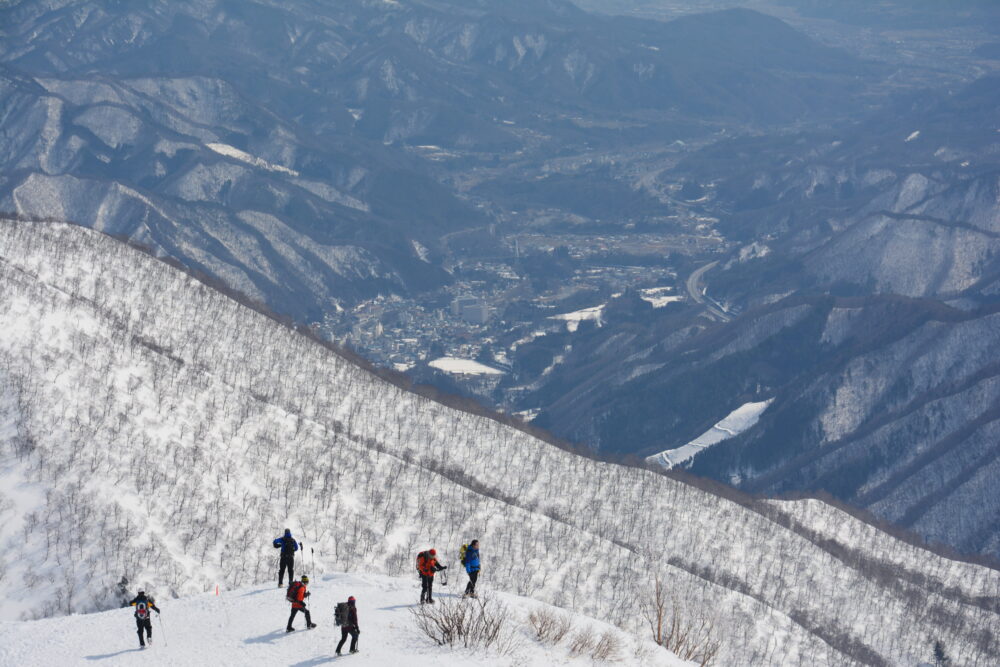 冬の谷川岳の天神尾根を歩く登山者たちと水上温泉街