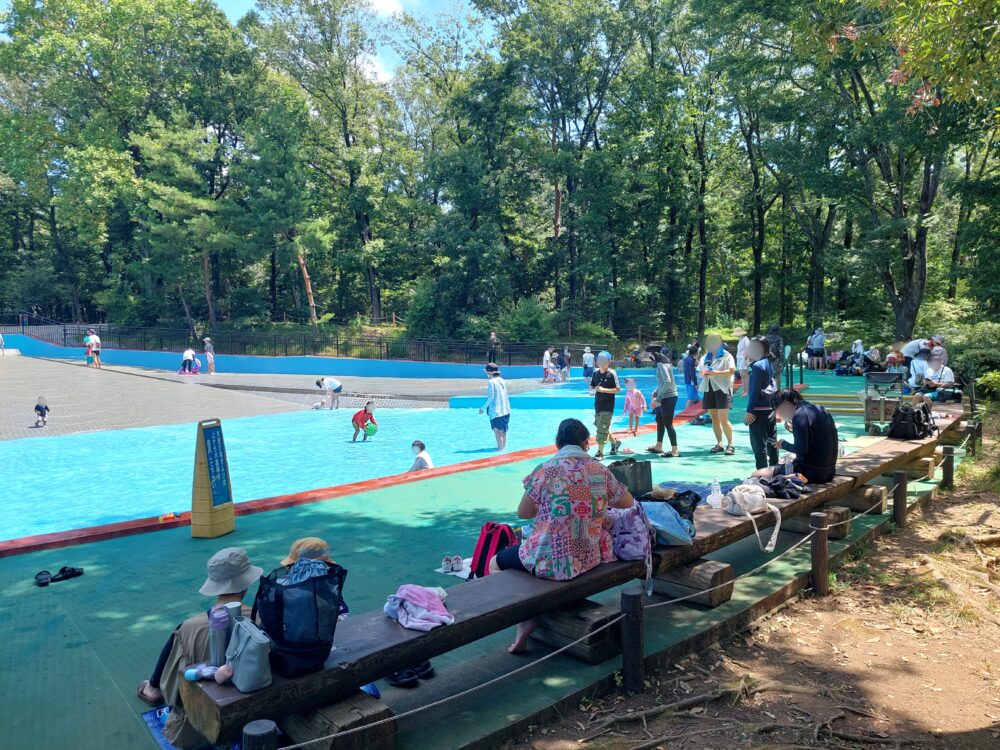 国営武蔵丘陵森林公園の水遊び場周りのベンチと遊んでいる人々