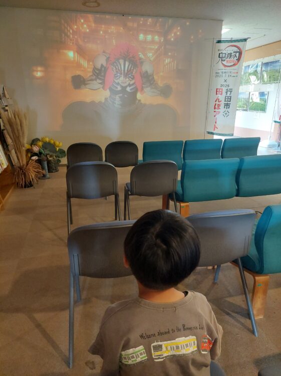 古代蓮会館(行田タワー)の1階で放映されている映画鬼滅の刃の予告編を見る子供