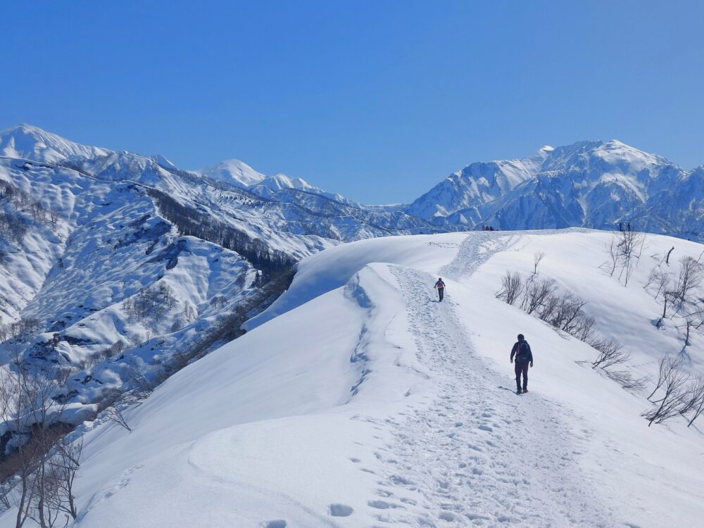 雪の大力山山頂から眺めた越後三山と登山者