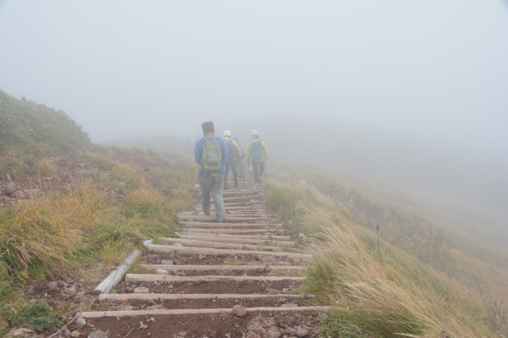 栗駒山のガスに包まれた登山道を下山する登山者