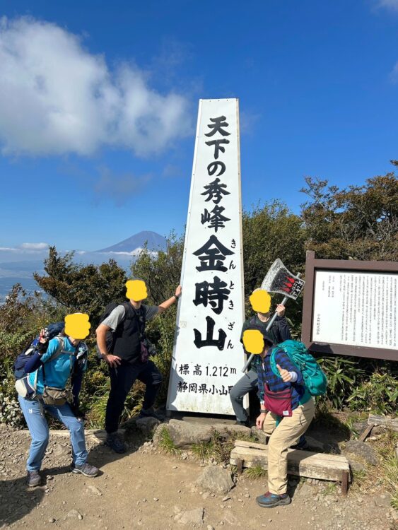 金時山山頂の山頂標識と富士山で記念撮影する4人の登山者